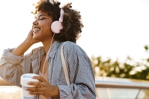 Smiling woman wearing pink headphones and holding a coffee cup, enjoying music outdoors; representing joy, self-care, and mental health awareness in women with ADHD
