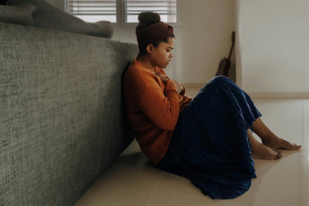 Young woman sitting on the floor feeling overwhelmed with anxiety and stress indoors.